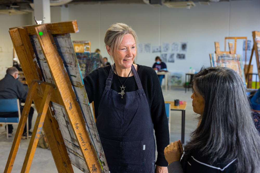 Gillian painting on a canvas discussing her work with a friend