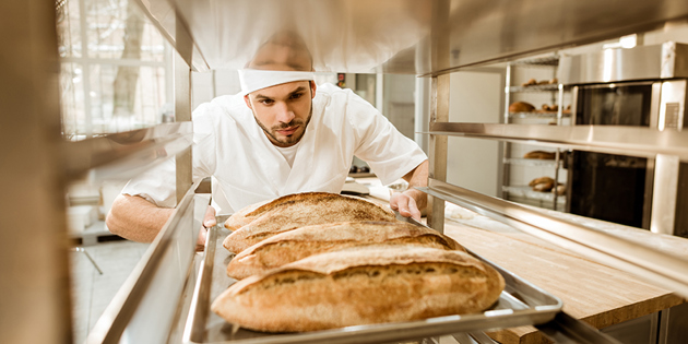 Professional Baker Putting Trays Of Fresh Bread